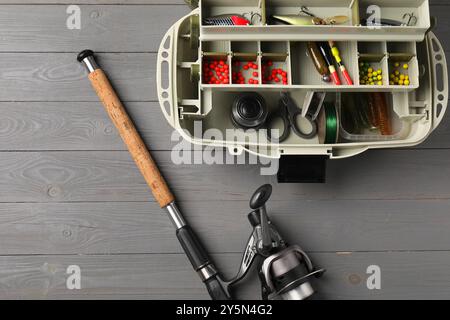 Différents tacles de pêche dans la boîte et la canne avec moulinet tournant sur la table en bois gris, vue de dessus. Espace pour le texte Banque D'Images