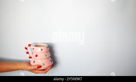 Tasse en forme d'arbre de Noël rose avec des points coloful dans la main des femmes avec copyspace, fond de carte de noël Banque D'Images