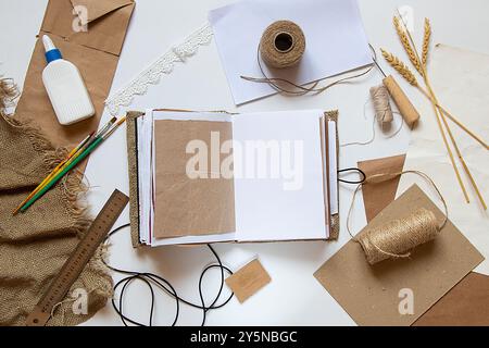 Un carnet fait maison repose sur la table et à côté se trouvent des papiers, de la colle, des fils et des pinceaux, un carnet fait main sur la table Banque D'Images