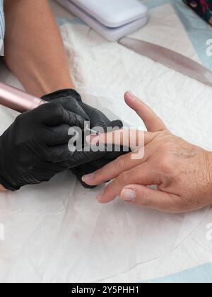 Une manucure nettoie la cuticule et les résidus de peinture des ongles d'une femme avec une perceuse à ongles électrique avec un mill. Banque D'Images