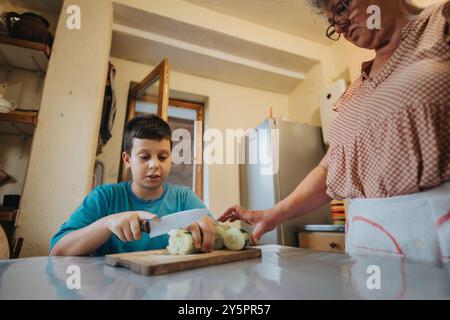 Jeune garçon apprenant à cuisiner avec grand-mère dans la cuisine rustique Banque D'Images