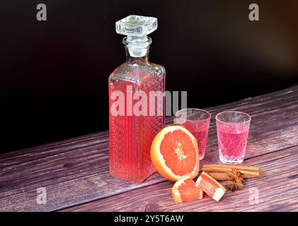 Liqueur de pamplemousse aux épices sur une table en bois, alcool maison fort dans une carafe en cristal et deux verres à dose à la cannelle et à l'anis. Gros plan Banque D'Images