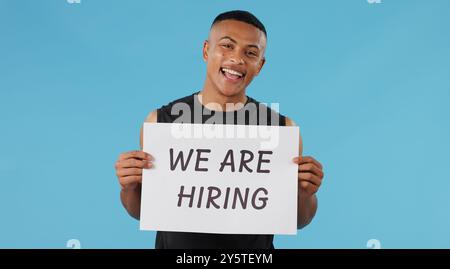 Homme, conseil et embauche en portrait de studio avec sourire, fitness et signe d'onboarding par fond bleu. Entraîneur personnel, affiche heureuse et présente avec Banque D'Images