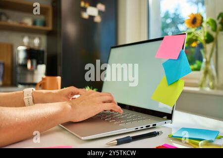 Femme travaillant à partir du bureau à domicile tapant sur le clavier d'ordinateur portable avec des notes adhésives colorées et de la papeterie sur le bureau Banque D'Images