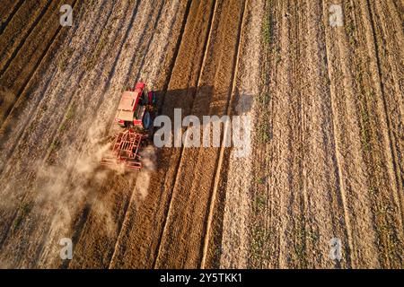 Tracteur rouge travaillant dans les champs agricoles, cultivant et labourant le sol sec, vue aérienne. Concept agroalimentaire. Concept de petite agriculture Banque D'Images