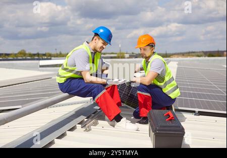 Ouvriers techniciens assis sur le toit et installant des panneaux solaires pour une énergie durable Banque D'Images