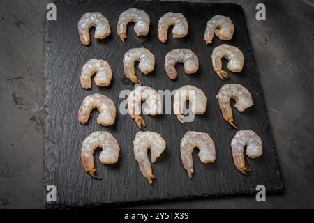 Crevettes crues disposées en rangées sur un panneau de mica noir sur un fond sombre. Photo de haute qualité Banque D'Images