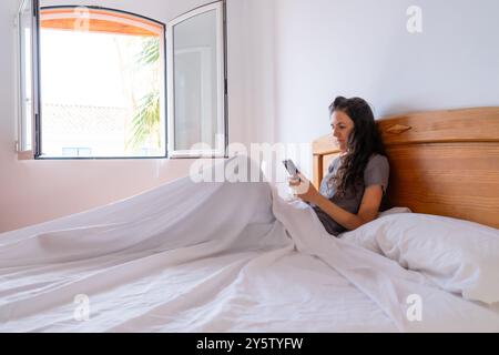 Femme caucasienne regardant un téléphone portable au lit pendant la journée Banque D'Images