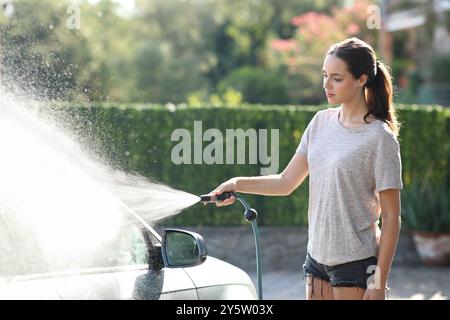 Femme sérieuse lavant la voiture avec de l'eau en utilisant Hosepipe à la maison Banque D'Images