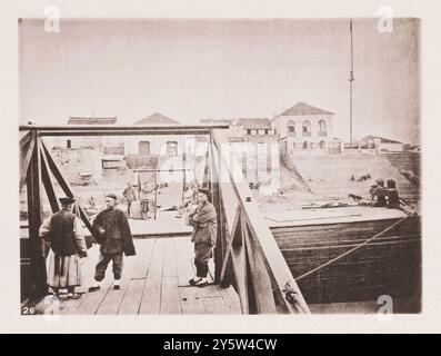 Photo vintage du quai, Jiujiang. Illustrations de la Chine Qing, 1875 les bâtiments à l'arrière-plan de cette photo comprennent la maison et les bureaux de MM. Russell et Co., une firme dont les splendides bateaux à vapeur ont grandement contribué à développer le trafic sur le Yangtze. Au premier plan, nous voyons une partie d'une passerelle flottante utilisée par les bateaux à vapeur pour débarquer les passagers et les marchandises. Sur le débarcadère, deux assistants chinois supervisent le déchargement des manufactures étrangères en balles. Ces balles sont suspendues entre deux coolies, et transportées sur un poteau de bambou ; le nombre est passé dans le wa Banque D'Images