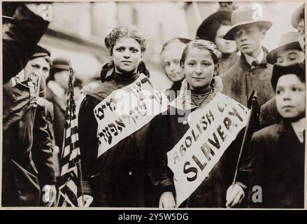 Protestation contre le travail des enfants dans un défilé du travail. ÉTATS-UNIS. La photographie du 1er mai 1909 montre un portrait en demi-longueur de deux filles portant des banderoles avec le slogan « ABOLIR L'ESCLAVAGE DES ENFANTS !! » En anglais et en yiddish, l'un portant le drapeau américain ; les spectateurs se tiennent à proximité. Probablement pris lors de la parade de travail du 1er mai 1909 à New York. Banque D'Images