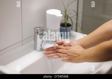 Femme se lavant les mains dans l'évier de salle de bain à la maison vérifiant la température touchant l'eau courante avec la main Banque D'Images