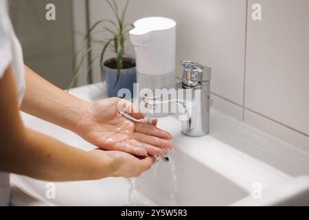 Femme se lavant les mains dans l'évier de salle de bain à la maison vérifiant la température touchant l'eau courante avec la main Banque D'Images