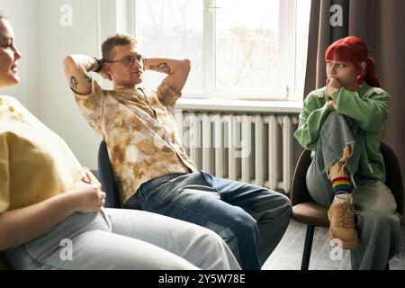 Groupe décontracté de trois amis assis dans le salon bavarder et se détendre, profiter de la conversation décontractée, et être à l'aise avec l'autre couple sur le canapé et la fille en sweat à capuche vert Banque D'Images