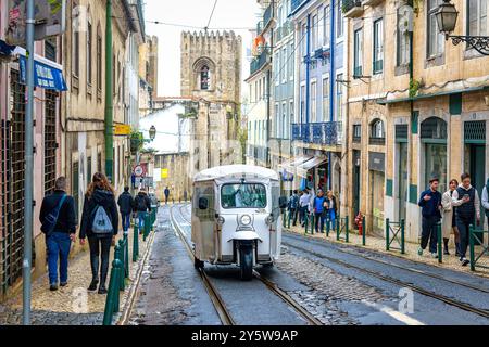 Lisbonne, Portugal - 19 septembre 2024 : des gens et un tricycle circulent dans une rue étroite du quartier de la vieille ville. Banque D'Images