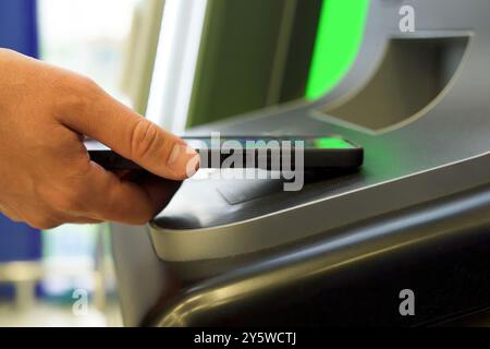 Un homme retire de l'argent d'un guichet automatique en utilisant son téléphone portable via un terminal NFC Banque D'Images