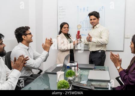 Un jeune homme d'affaires célèbre avoir remporté un prix tandis qu'une collègue heureuse le félicite pour sa réussite professionnelle. Ils sont entourés de diverses entreprises Banque D'Images