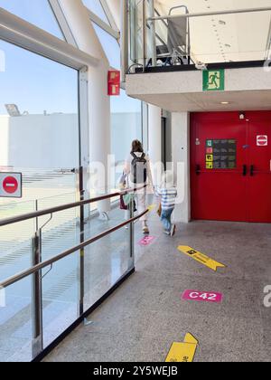Palma, Espagne, 11 juillet 2024 : une image verticale d'une mère et de son fils marchant à l'intérieur de l'aéroport PMI, suivant plusieurs flèches de guidage sur le sol Banque D'Images