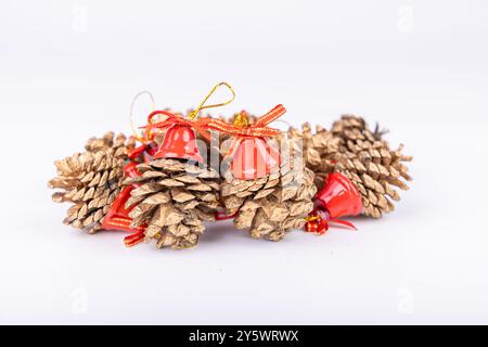 Les pommes de pin avec cloches rouges et ruban doré se placent sur un fond blanc, offrant une décoration de Noël festive et élégante Banque D'Images