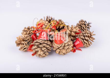 Pommes de pin avec cloches rouges et un ruban doré sur fond blanc. Une touche festive pour Noël et les vacances Banque D'Images