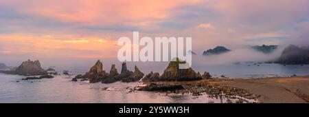 Une large photo panoramique 3:1 d'un lever de soleil brumeux sur la plage de Gueirua, une petite baie de galets qui est remarquable pour ses beaux paysages. À l'extrémité est de th Banque D'Images