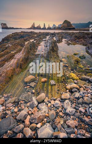 Un lever de soleil sur la plage de Gueirua, une petite baie de galets qui est remarquable pour ses beaux paysages. À l'extrémité est de la plage, une rangée d'îlots rocheux pointus Banque D'Images