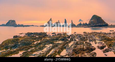 Une photo panoramique 2:1 d'un lever de soleil brumeux sur la plage de Gueirua, une petite baie de galets qui est remarquable pour ses beaux paysages. À l'extrémité est du bea Banque D'Images