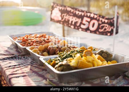 Table de pique-nique extérieure décorée pour une célébration d'anniversaire avec une bannière 'Happy 50th Birthday' et des plateaux de plats délicieux dans la lumière chaude du soleil, Floride, États-Unis Banque D'Images