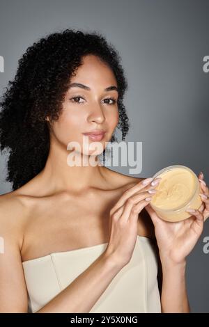 Une femme magnifiquement habillée affiche élégamment son produit de soins de la peau avec confiance et flair. Banque D'Images