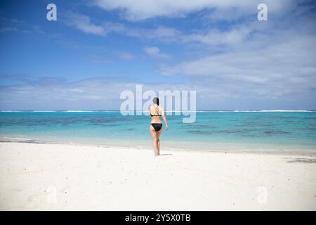 Une femme se tient debout sur une plage immaculée regardant l'océan turquoise sous un ciel bleu, Titikaveka, Rarotonga, Îles Cook Banque D'Images