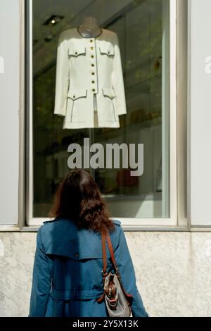 Une femme en manteau bleu regarde une veste blanche exposée dans une vitrine. Banque D'Images