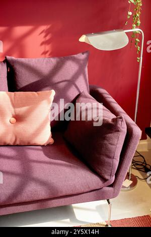 Un fauteuil violet moderne avec un coussin rose contre un mur rouge vif, avec des ombres végétales et un lampadaire blanc. Banque D'Images