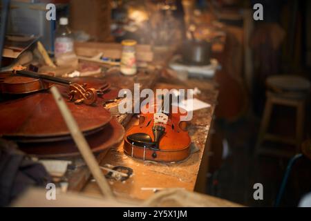 Un violon et un arc reposant sur un établi encombré dans un atelier de violoniste entouré d'outils et de copeaux de bois. Banque D'Images