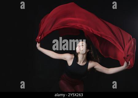 jeune femme latino dansant vêtue de rouge et noir sur fond sombre Banque D'Images