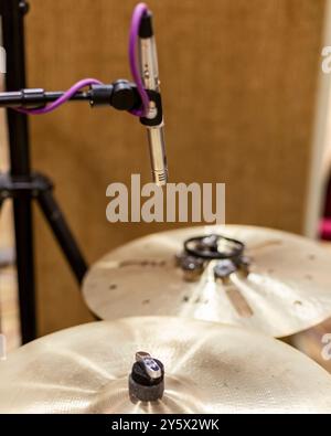 Gros plan d'un set de batterie avec des cymbales et un pied de microphone en mise au point, placé sur un fond chaud flou. Banque D'Images