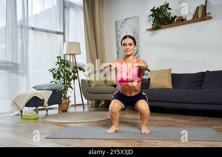 Une jeune femme brune déterminée avec une petite stature exécute des squats à la maison, démontrant son engagement envers la forme physique et la santé. Banque D'Images