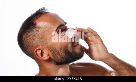 Portrait de beau homme barbu souriant appliquant un masque nasal pour le nettoyage des pores isolé sur fond blanc de studio. Vue latérale Banque D'Images
