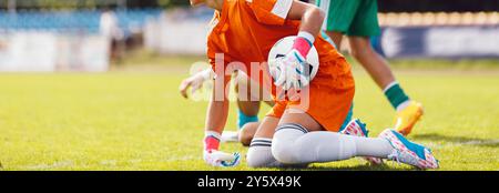 Gardien de but de football attrapant un ballon lors d'un match de ligue. Ligue de football pour les jeunes joueurs. Gardien de but de football tenant une balle en gants Banque D'Images