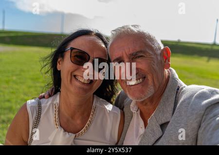 beau couple d'âge moyen heureux et souriant habillé élégamment prenant un selfie lors d'une cérémonie à la campagne Banque D'Images
