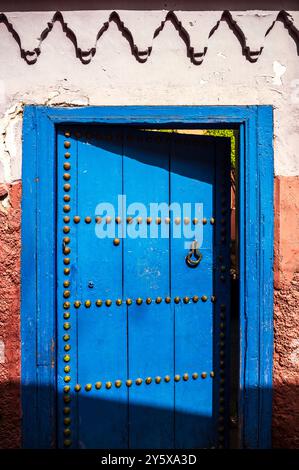 Une porte bleue, située à Marrakech, au Maroc, avec le soleil rude du désert projetant des ombres frappantes à travers le cadre Banque D'Images