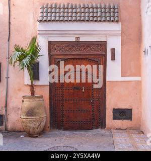 Une grande porte en bois, située dans le souq de Marrakech. Il y a un pot de plante de tourbière avec un palmier dedans, à côté de la porte Banque D'Images