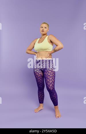 Une jeune femme chauve vêtue de vêtements vibrants se tient confiante, frappant une pose audacieuse dans un studio. Banque D'Images