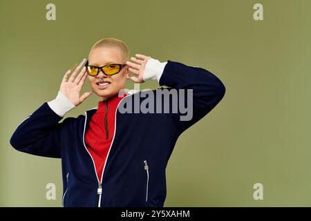 Cette jeune femme chauve dynamique pose de manière ludique dans une tenue colorée avec un sourire confiant. Banque D'Images