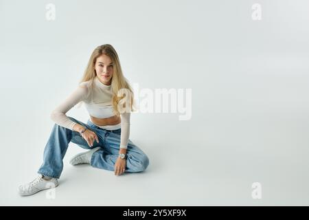 Une jeune femme à la mode s'assoit confortablement sur le sol, mettant en valeur son style et sa confiance. Banque D'Images