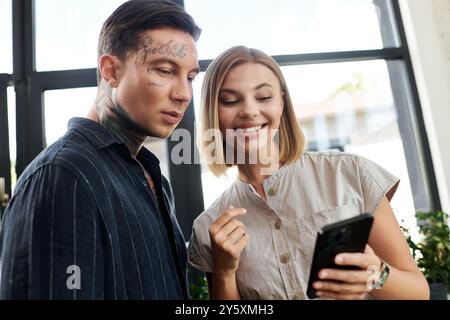 Deux collègues s’engagent avec enthousiasme, riant et discutant sur un téléphone portable au bureau. Banque D'Images