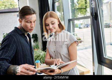 Deux jeunes collègues discutent des idées et examinent des documents tout en se tenant debout près de grandes fenêtres. Banque D'Images