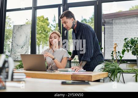 Deux collègues s'engagent dans une discussion animée tout en travaillant sur un ordinateur portable à leur bureau. Banque D'Images