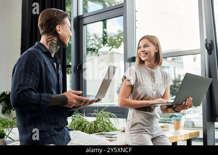 Deux collègues s'engagent dans une conversation joyeuse tout en travaillant sur des ordinateurs portables au bureau. Banque D'Images