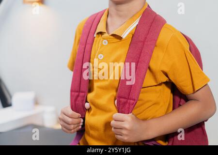 Gros plan d'un jeune étudiant tenant une sangle de sac à dos, vêtu d'une chemise jaune, dans une salle de classe. Capture l'essence de la vie scolaire et de l'éducation Banque D'Images