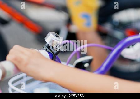 Une main d'enfant sur le guidon d'un vélo violet, mettant en valeur l'activité et le jeu en plein air. Une cloche argentée est attachée à la poignée, soulignant le bi Banque D'Images